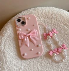 an iphone case with pearls and pink bows on it next to a necklace that is laying on top of a white towel