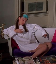 a woman sitting on top of a white couch next to a table filled with books