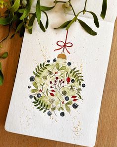 an ornament with berries and leaves is hanging from a card on a table