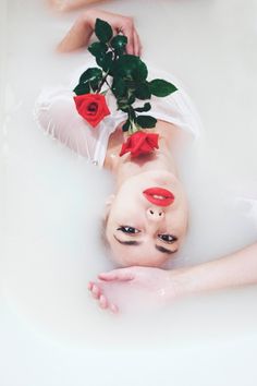 a woman laying in a bathtub with roses on her head and eyes painted red