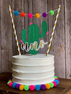 a white cake with a green cactus on top and colorful pom - poms around it