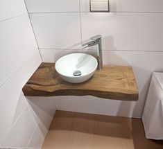 a white bowl sink sitting on top of a wooden counter next to a toilet paper dispenser