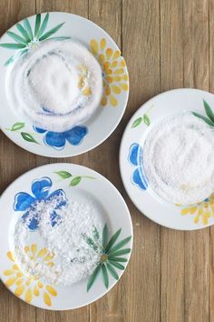 three plates with different types of powdered sugar on them, sitting on a wooden table