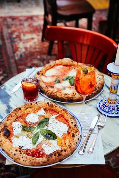 two pizzas sitting on top of a table next to glasses of wine and silverware