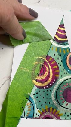 someone is cutting out an origami christmas tree with green and purple paper on it