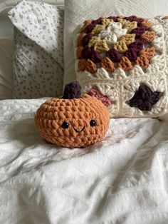 a crocheted pumpkin sitting on top of a bed next to a decorative pillow