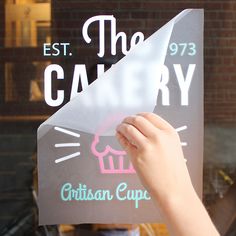 a person holding up a sign in front of a store window that says the cakery