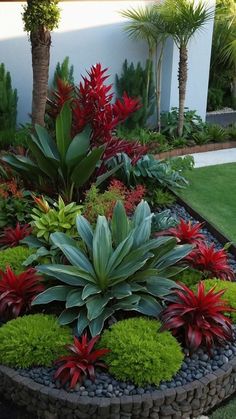 a garden filled with lots of green and red flowers next to a white wall on top of grass