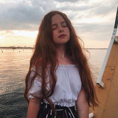 a girl with long hair standing on the edge of a boat looking at the water