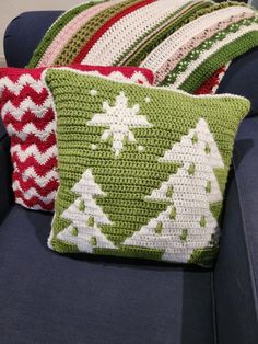 three crocheted christmas trees pillows sitting on a blue couch next to each other