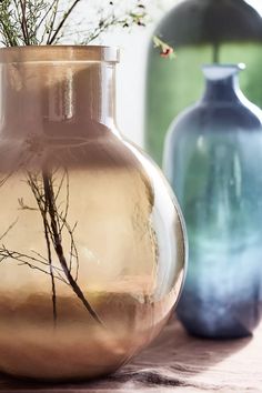 two vases with branches in them sitting on a table next to each other,