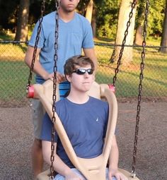 two boys are sitting on swings in the park, one is wearing sunglasses and the other has a blue t - shirt