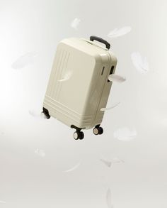 a white piece of luggage flying through the air with feathers in the sky behind it