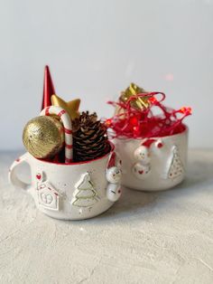 two white mugs filled with christmas decorations