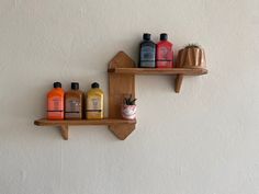 two wooden shelves with bottles and soaps on them against a white wall in the corner