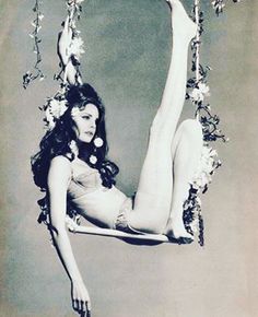 an old photo of a woman on a swing with flowers in her hair and stockings