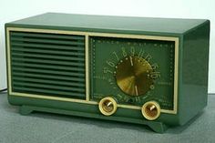 an old fashioned green and gold radio sitting on the floor in front of a white wall