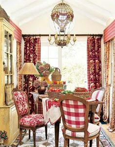 the dining room is decorated with red and white plaid furniture, china cabinet, chandelier