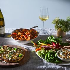 a table topped with plates of food next to a bottle of wine and a bowl of salad