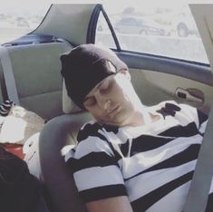 a young man sitting in the back seat of a car wearing a hat and striped shirt