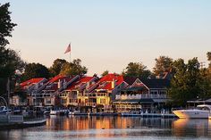 several boats are docked in the water near some houses and trees with an american flag flying above them