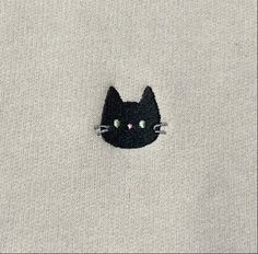 a black cat with green eyes peeking out from the back of a white shirt that has been embroidered onto it