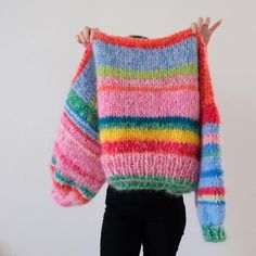 a woman is holding up a multicolored sweater with her hands in the air