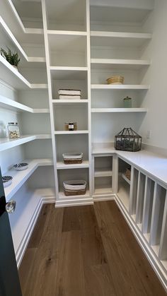 an empty walk - in closet with white shelving and wood flooring is shown