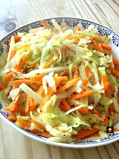 a bowl filled with coleslaw and carrots on top of a wooden table