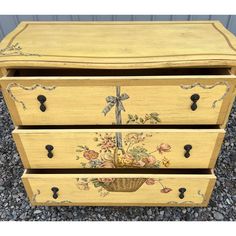 an old dresser with flowers painted on the front and sides, sitting in graveled area