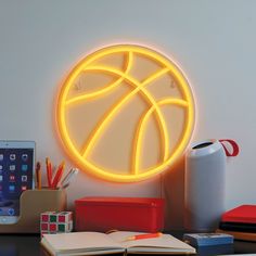 an illuminated basketball ball sits on a desk next to a cell phone and pencils