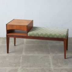 a wooden bench with a green cushion on it and a white wall in the background