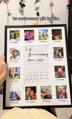 a person holding up a framed calendar with pictures on it and flowers in the background