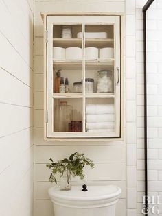 a white toilet sitting in a bathroom next to a cabinet filled with bottles and towels