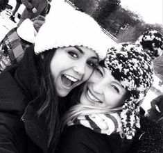 two young women are smiling and posing for the camera while wearing knitted hats with pom poms