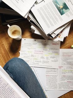 a pile of papers sitting on top of a wooden floor next to a cup of coffee