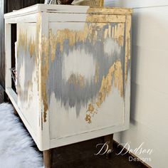 an old dresser with gold paint on it and white furnishing in the background