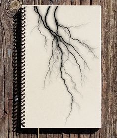 a spiral bound notebook with black and white drawing of lightning strikes on the cover, against a weathered wood background