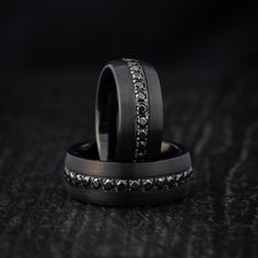 two wedding rings with black diamonds on top of each other in front of a dark background