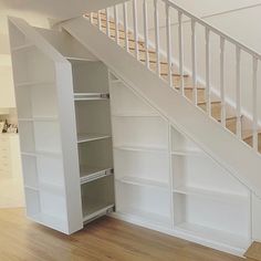 an open bookcase under the stairs in a house with wood floors and white walls