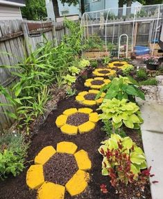 a garden with yellow and black flowers in the center, surrounded by plants on either side