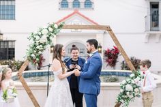 a bride and groom exchange vows in front of their wedding ceremony arch with flower arrangements