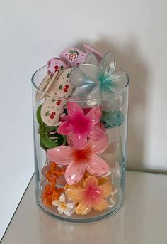 a glass container filled with lots of different colored plastic flowers on top of a table