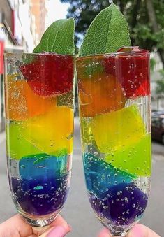 two people holding up wine glasses filled with colored liquid and green leaf on the top