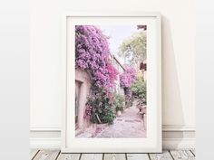 a white framed photograph with purple flowers on the side of a building and wood floor