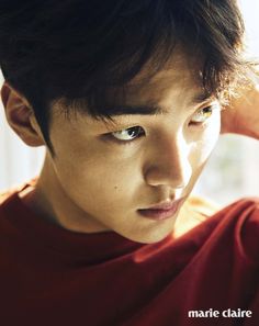 a young man with dark hair and blue eyes is looking at the camera while wearing a red t - shirt