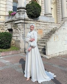 a woman standing in front of an old building wearing a white dress and head scarf