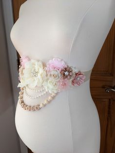 a white mannequin with pink flowers and pearls on it's belt, sitting in front of a wooden door