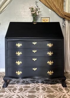 a black dresser with gold leaf handles and drawers in a room that has curtains on the windows