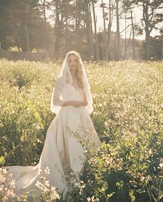 a woman in a white wedding dress and veil standing in the middle of a field